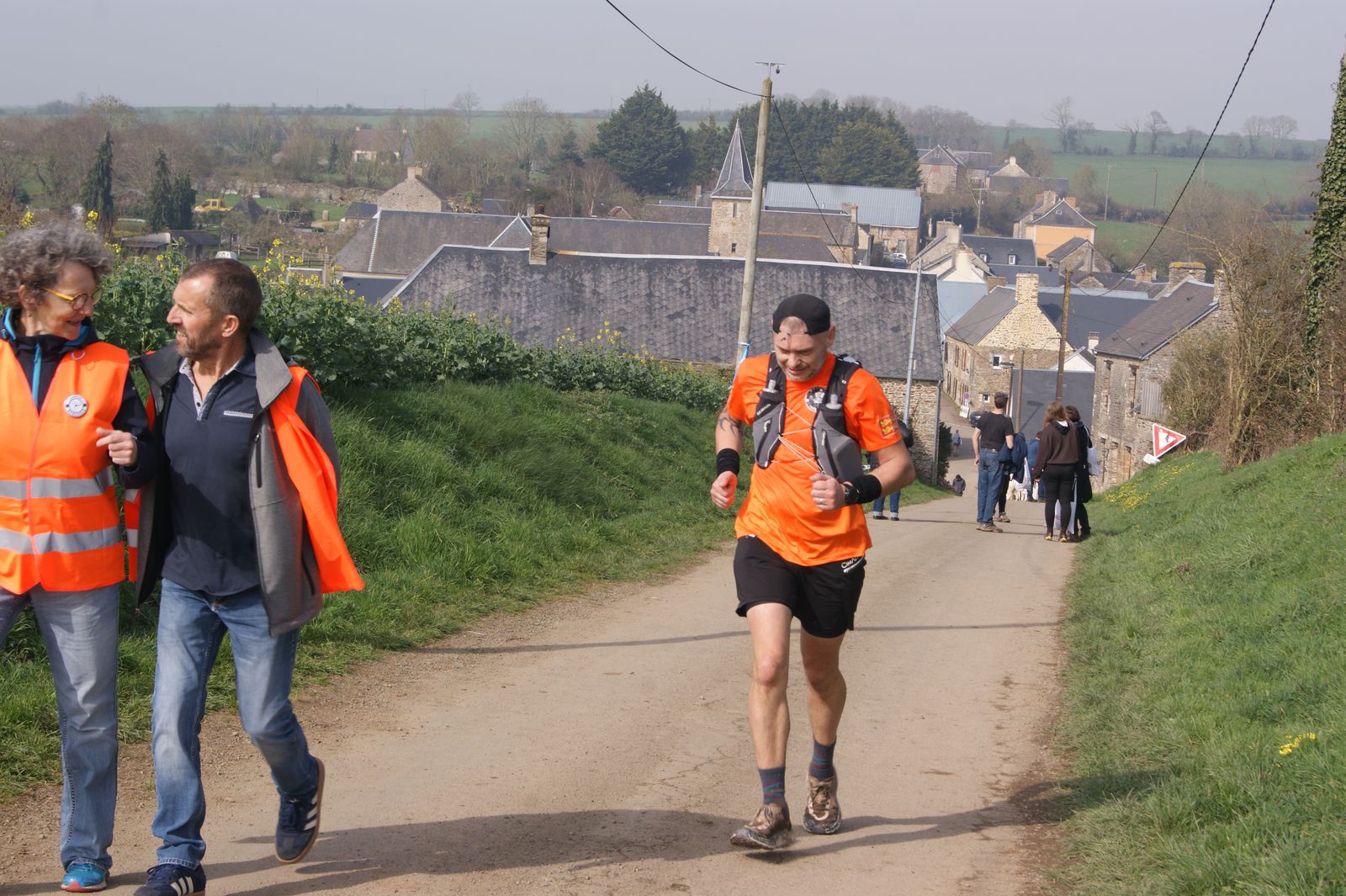 Bénévoles en gilet orange aux côtés d'un coureur, au-dessus de Hamars